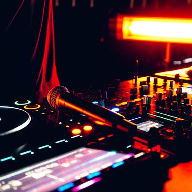 Ein DJ-Pult mit verschiedenen Reglern und Tasten, beleuchtet von rotem Licht. Ein Mikrofon liegt bereit für den Einsatz. | © Kleinwalsertal Tourismus eGen