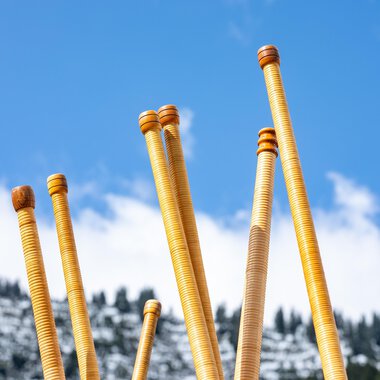 A group of people is playing alphorns on a terrace. In the background, sunny mountains and a clear blue sky can be seen. | © Kleinwalsertal Tourismus | Frank Drechsel