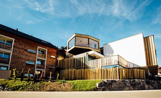 Ein modernes Gebäude mit Holzverkleidung und großen Fenstern. Es liegt in einer ruhigen Umgebung und hat eine ansprechende Architektur.