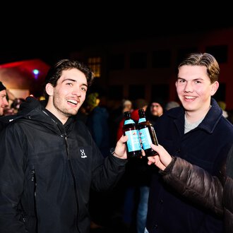 Eine festliche Veranstaltung mit einer großen Schneemann-Puppe und vielen feiernden Menschen. Bunte Lichter erhellen die Szene.