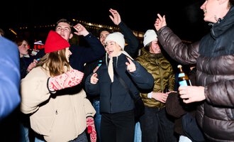 Eine Gruppe von Menschen feiert fröhlich in der Nacht. Sie tanzen und haben Spaß, während sie verschiedene warme Kleidung tragen.