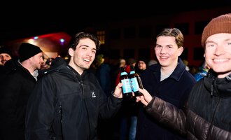 Eine festliche Veranstaltung mit einer großen Schneemann-Puppe und vielen feiernden Menschen. Bunte Lichter erhellen die Szene.