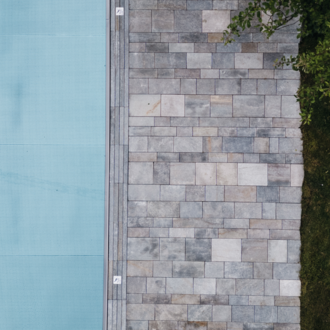 A modern designed outdoor area with a blue pool and a stone path. Next to it lies a green lawn and some foliage. | © Naturhotel Chesa Valisa