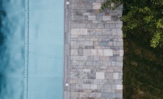 A modern designed outdoor area with a blue pool and a stone path. Next to it lies a green lawn and some foliage. | © Naturhotel Chesa Valisa