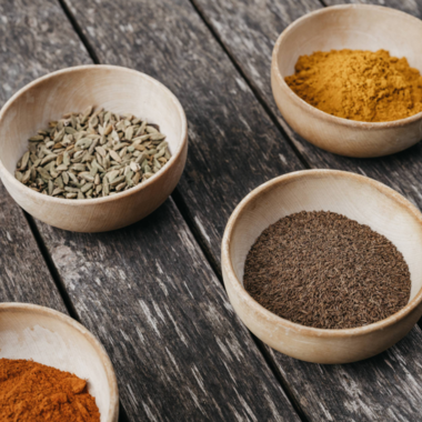 Four small bowls with various spices are placed on a wooden table. The colors of the spices range from orange to yellow to brown. | © Naturhotel Chesa Valisa