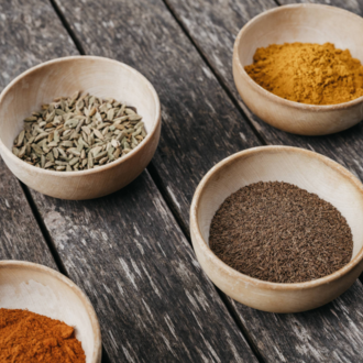Four small bowls with various spices are placed on a wooden table. The colors of the spices range from orange to yellow to brown. | © Naturhotel Chesa Valisa