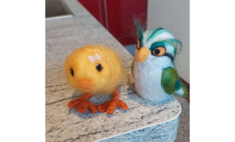 Ein gelbes, buntes Küken und ein gefilzter Vogel stehen nebeneinander auf einer grauen Oberfläche. Beide Figuren sind liebevoll gestaltet und zeigen lebendige Farben. | © Maria Möckel, Der Kleinwalsertaler Rosenhof