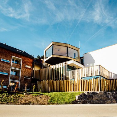 Ein modernes Gebäude mit Holzverkleidung und großen Fenstern. Die Architektur kombiniert traditionelle und zeitgenössische Elemente. | © Genuss- und Aktivhotel Sonnenburg | Andi Mayr