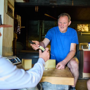 A man explains something while two people listen attentively. The scene takes place in a rustic interior. | © Kleinwalsertal Tourismus eGen - Fotograf: Oliver Farys