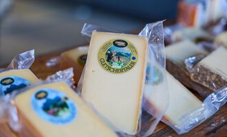 Eine Auswahl von verpacktem Käse auf einem Tisch. Der Käse hat verschiedene Etiketten und Verpackungen. | © Kleinwalsertal Tourismus | Oliver Farys