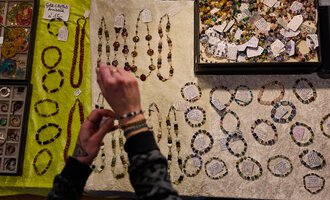 Ein Standsort mit verschiedenen Schmuckstücken aus Perlen und Steinen. Eine Person betrachtet die Halsketten und Armbänder auf einem hellen Tuch. | © Kleinwalsertal Tourismus | Oliver Farys