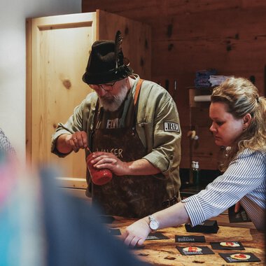 Ein Mann und eine Frau bereiten etwas in einer gemütlichen Küche vor. Der Mann trägt einen Hut und eine Schürze, während die Frau konzentriert arbeitet. | © Angela Lamprecht | Vorarlberg Tourismus