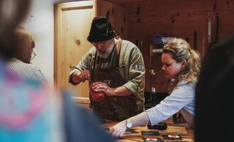 Ein Mann und eine Frau bereiten etwas in einer gemütlichen Küche vor. Der Mann trägt einen Hut und eine Schürze, während die Frau konzentriert arbeitet. | © Angela Lamprecht | Vorarlberg Tourismus