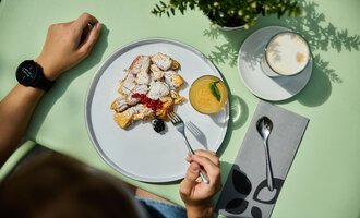 Ein Teller mit süßem Gebäck, Puderzucker und Beeren, dazu ein Glas Saft und eine Tasse Kaffee. Die Szene ist auf einem grünen Tisch. | © Kleinwalsertal Tourismus | Oliver Farys
