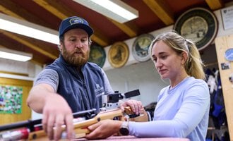 Ein Mann zeigt einer Frau, wie man ein Luftgewehr benutzt. Beide wirken konzentriert in einer sportlichen Umgebung. | © Kleinwalsertal Tourismus | Oliver Farys