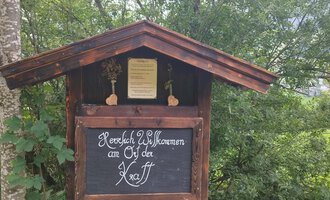 Ein herzliches Willkommensschild an einem Holzgebäude in der Natur. Umgeben von Bäumen und grüner Landschaft. | © Nicole Lughammer