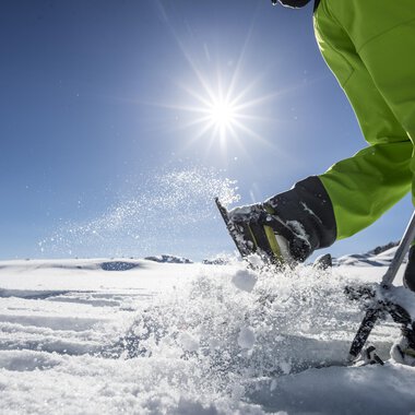 Ein sonniger Tag im Schnee mit einem Menschen, der mit einem Skistöck im Schnee arbeitet. Im Hintergrund ist eine weitere Person zu sehen. | © Kleinwalsertal Tourismus | Dominik Berchtold
