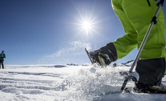 Ein sonniger Tag im Schnee mit einem Menschen, der mit einem Skistöck im Schnee arbeitet. Im Hintergrund ist eine weitere Person zu sehen. | © Kleinwalsertal Tourismus | Dominik Berchtold