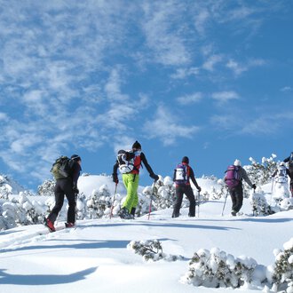 A group of people is hiking through snow-covered landscapes. The sky is clear and blue. | © Kleinwalsertal Tourismus | Frank Drechsel