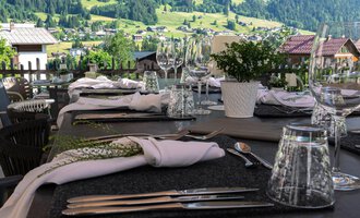 A beautifully set table on a terrace overlooking green hills. Umbrellas provide shade for the guests. | © Genuss- & Aktivhotel Sonnenburg