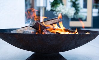 A rustic fire in a round fire pit. The flames flicker over the logs and create a cozy atmosphere. | © Genuss- & Aktivhotel Sonnenburg