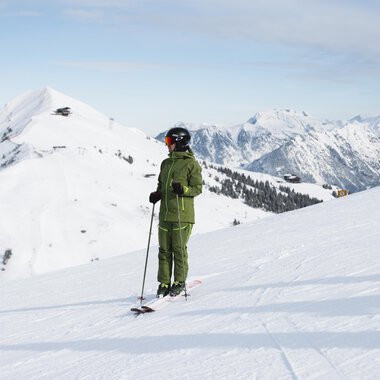 Ein Skifahrer steht auf einem verschneiten Berggipfel und schaut auf die umliegenden Berge. Der Himmel ist klar und die Landschaft ist winterlich schön. | © OBERSTDORF·KLEINWALSERTAL BERGBAHN