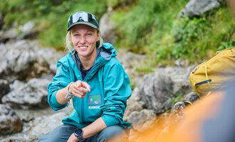 Eine Eule mit intensiven orangefarbenen Augen und einem detailreichen Gefieder. Der Hintergrund ist dunkel, wodurch die Eule kontrastreich hervortritt. | © Kleinwalsertal Tourismus | Oliver Farys
