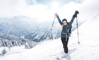 Ein Skifahrer in einem blauen Anzug fährt durch frischen, pulvrigen Schnee. Im Hintergrund sind schneebedeckte Berge und ein klarer blauer Himmel zu sehen.