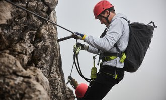 Ein Kletterer ist an einer Felswand befestigt und konzentriert sich auf seine Technik. Im Hintergrund ist ein weiterer Kletterer zu sehen, während eine neblige Atmosphäre herrscht. | © Bergschule Kleinwalsertal | Oliver Farys