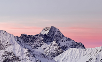 Eine majestätische Berglandschaft mit schneebedeckten Gipfeln und einem sanften rosa Himmel. Die Szenerie strahlt Ruhe und natürliche Schönheit aus.
