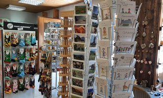 Ein gemütlicher Laden mit einem Präsentationsstand für Postkarten und Souvenirs. Im Hintergrund sind bunte Socken und andere Geschenkartikel zu sehen. | © Abler Mitbringsel Riezlern | Veronika Senn
