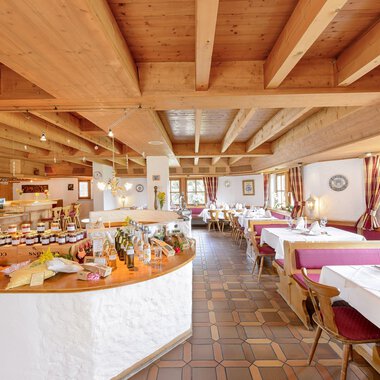 A cozy restaurant with a beamed ceiling and friendly atmosphere. Tables are set, and a buffet with various delicacies is visible. | © Alpengasthof Hörnlepass | Monschau Michael