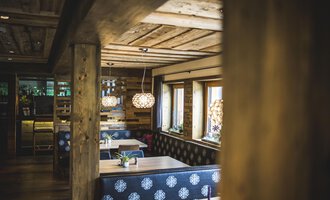 A cozy interior design with wooden beams and a stylish, modern design.  
There are plants on the table and there are striking lamps as well as windows with natural light. | © Das Alphotel Hirschegg Hotel GmbH | Dominik Berchtold