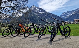 Eine Gruppe von Fahrrädern steht auf einem gepflasterten Weg vor einer beeindruckenden Berglandschaft. Der Himmel ist klar und es gibt noch Schnee auf den Gipfeln. | © Austrian Ski- & Service Ranch | Trixi Leitner