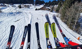 Eine verschneite Skipiste mit Bäumen und Hütten im Hintergrund. Skier sind im Vordergrund zu sehen. | © Austrian Ski- & Service Ranch | Trixi Leitner