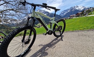 Ein modernes Mountainbike steht auf einem Weg inmitten einer malerischen Berglandschaft. Im Hintergrund sind schneebedeckte Berge und grüne Wiesen zu sehen. | © Austrian Ski- & Service Ranch | Trixi Leitner