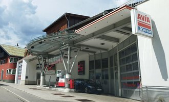 A modern gas station with a large canopy is located on a quiet street. In the background, residential buildings and a cloudy sky can be seen. | © Kleinwalsertal Tourismus | N. Lughammer