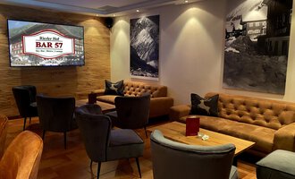 An elegant bar with comfortable seating and warm wooden tones. Beautiful black-and-white photographs hang on the walls. | © Hotel Riezler Hof | M. Hasterok