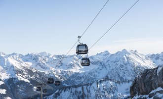 A cable car rides over snow-covered mountains. The sky is clear and blue, the landscape is impressive. | © OBERSTDORF · KLEINWALSERTAL BERGBAHNEN