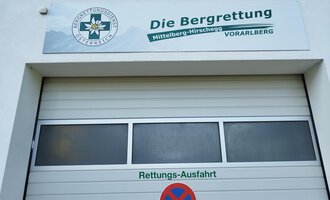 Ein Garagentor mit dem Schild der Bergrettung in Mittelberg-Hirschegg, Vorarlberg. Das Schild enthält das Logo und Informationen zur Rettungsausfahrt. | © Kleinwalsertal Tourismus