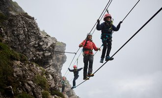 Eine Gruppe von Kletterern zieht an einem Seil in den Bergen. Alle tragen Helme und Sicherungsgurte, während sie an einer Felswand arbeiten. | © Bergschule Walser Klettersteig @Bergschule Kleinwalsertal Oliver Farys