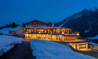 Ein modernes Gebäude in den Bergen, umgeben von Schnee und einem klaren, blauen Himmel. Die warmen Lichter des Hauses schaffen eine einladende Atmosphäre in der Dämmerung. | © Hotel Birkenhöhe | Fotos GA Service Salzburg