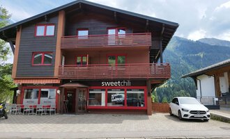 Ein modernes Gebäude mit zwei Etagen in den Bergen. Das Erdgeschoss beherbergt das Restaurant "sweetchill" mit großen Fenstern. | © Kleinwalsertal Tourismus | N. Lughammer