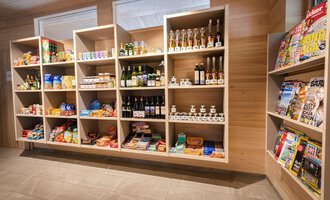 A well-organized sales shelf with groceries, beverages, and magazines. The shelves are made of wood and offer a variety of products. | © Campingplatz Vorderboden GmbH | Marion Schwendiger