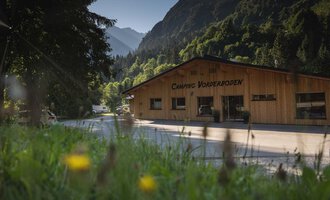 Ein Holzgebäude mit dem Schriftzug "Camping Vorberdoden" in einer grünen Umgebung. Im Hintergrund sind Berge und Bäume zu sehen. | © Campingplatz Vorderboden GmbH | Marion Schwendiger