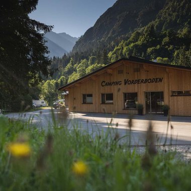 A wooden building with the inscription "Camping Vorberdoden" in a green environment. In the background, mountains and trees can be seen. | © Campingplatz Vorderboden GmbH | Marion Schwendiger