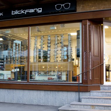 An optical shop with large windows and a selection of sunglasses. The store has a sign that says "blickfang" and has a modern design. | © Blickfang | Michael Stumpe