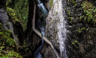 A picturesque gorge with steep cliffs and a flowing brook. Lush greenery surrounds the area, creating a tranquil atmosphere. | © Breitachklamm | Dominik Berchtold