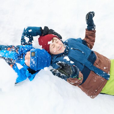 Ein Schlitten steht im Schnee, umgeben von schneebedeckten Bergen. Die Sonne strahlt im Hintergrund und erzeugt eine malerische Winterlandschaft. | © Kleinwalsertal Tourismus | Oliver Farys