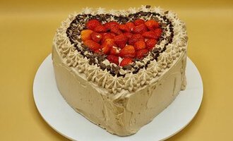 Eine herzförmige Torte mit einer cremigen Füllung, garniert mit Schokolade und frischen Erdbeeren. Der Hintergrund ist einfarbig und unterstreicht die Torte.